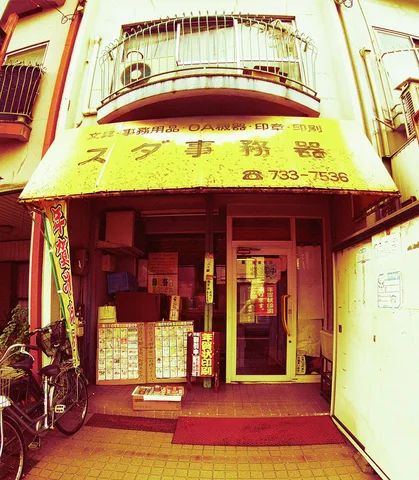 A faded yellow awning shelters a glass shop entrance beneath a curved upstairs balcony.
