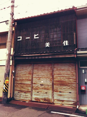 Rust-streaked shutters close a dark wooden storefront beside a utility pole and overhead wires.