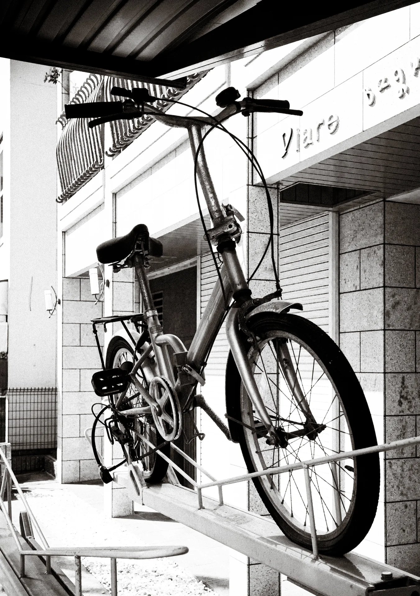 A bicycle rests on a raised ledge beneath an awning above pale chairs in black and white.