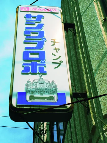 Bold blue characters and an illustrated machine fill a projecting white vertical sign.