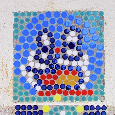Small blue, turquoise, white, and red circular tiles form a cartoon face on a pale wall.