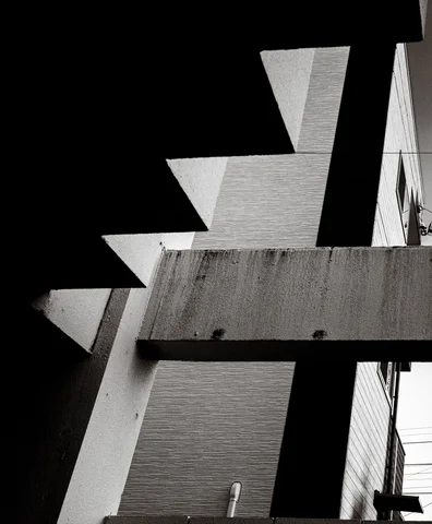 Angular concrete stair edges create alternating bright triangles and deep black shadows in black and white.