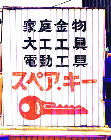 Black and red Japanese lettering and a large red key decorate a white corrugated shop sign.