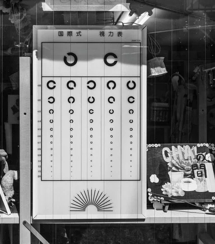 A black and white eye chart with descending broken circles hangs in a window beside printed advertisements.