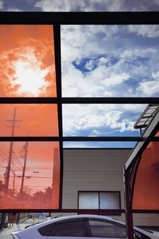 Dark window frames divide orange-tinted panes and reflections of blue sky and white clouds.
