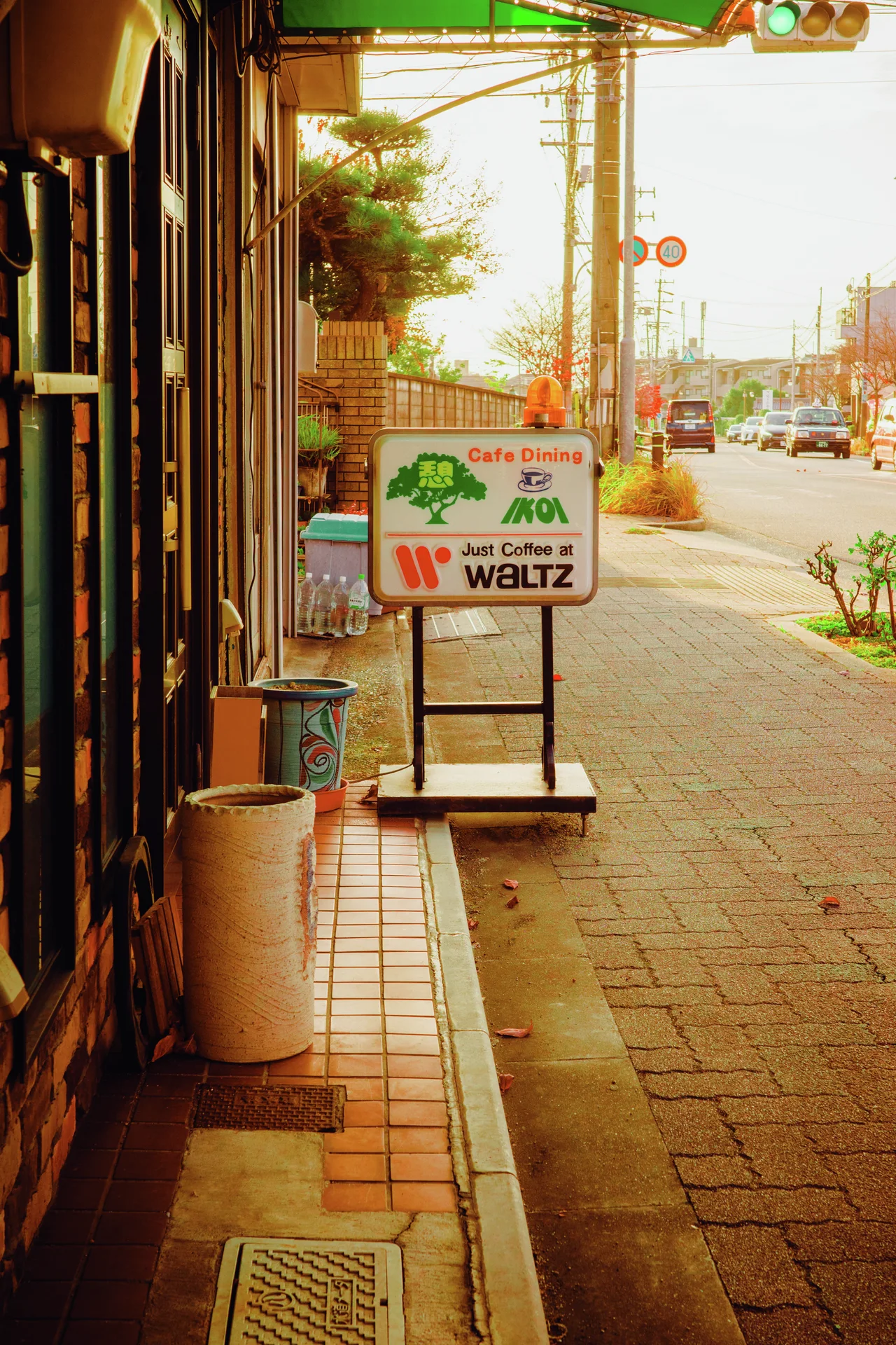 A freestanding cafe sign and white planter stand on a warmly lit sidewalk beside shop windows.