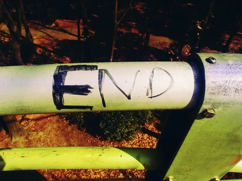 The handwritten word END appears on a pale metal railing above a sunlit wooded slope.