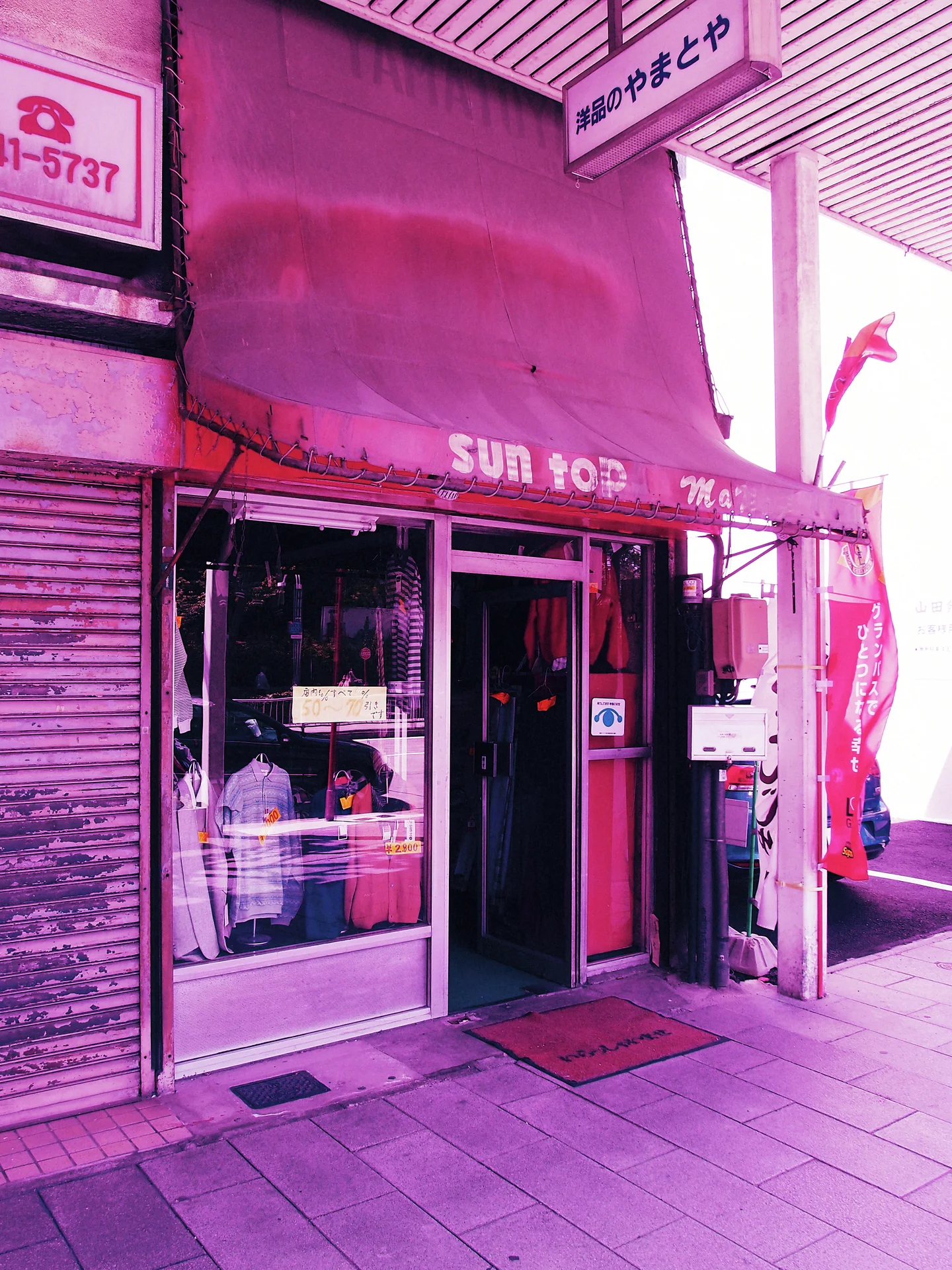 A pink awning shades a small glass-fronted shop entrance beneath a ribbed covered sidewalk.