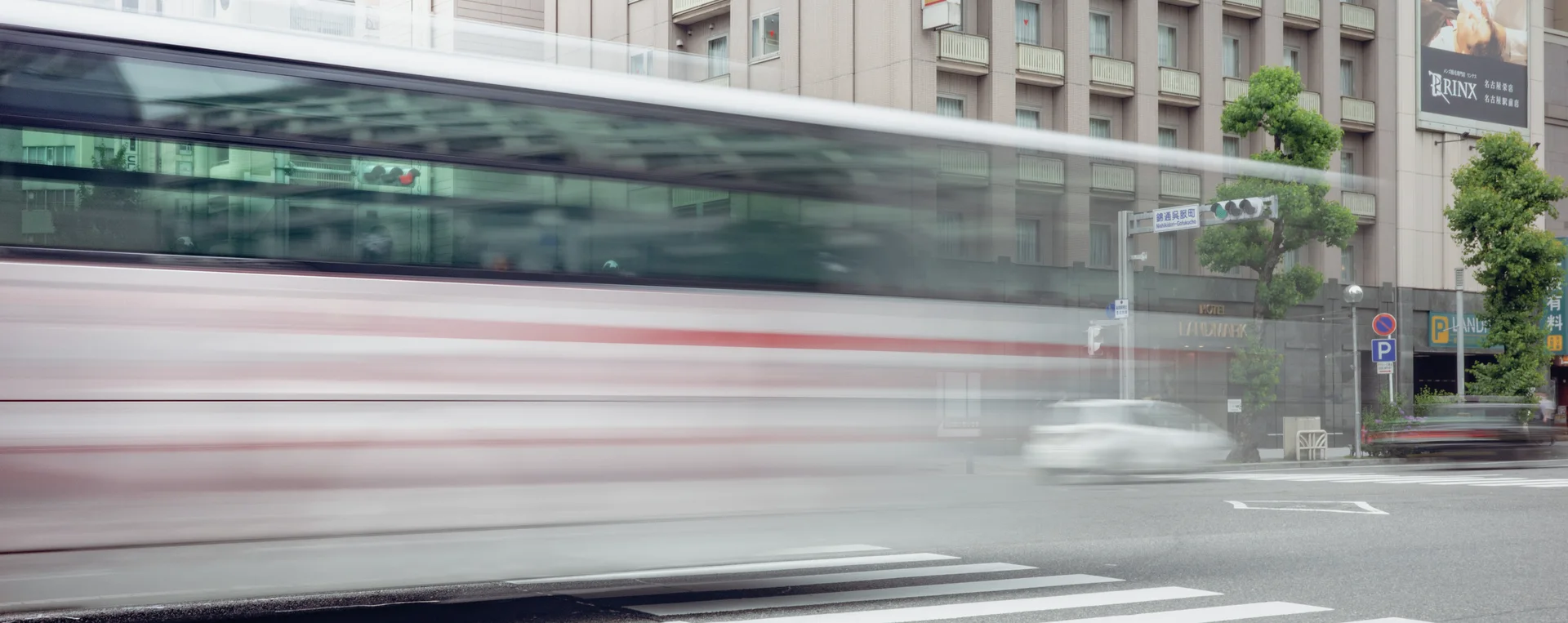 A passing bus appears horizontally blurred across a street before pale urban buildings.