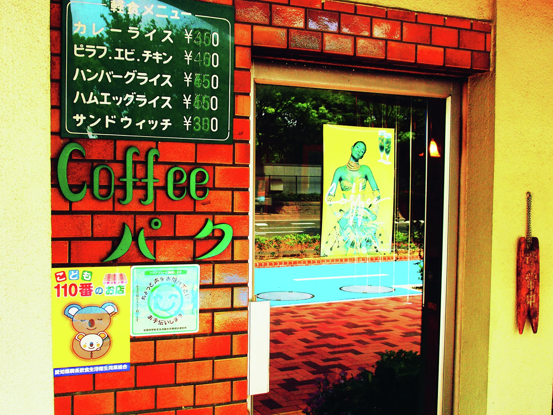 A handwritten green menu and raised Coffee lettering decorate red brickwork beside a reflective glass door.