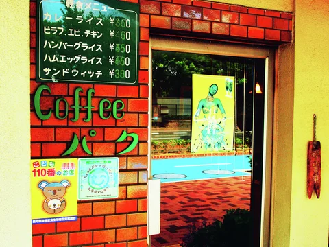 A handwritten green menu and raised Coffee lettering decorate red brickwork beside a reflective glass door.