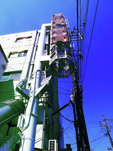 A decorative streetlight rises beside a white building and tangled wires against deep blue sky.