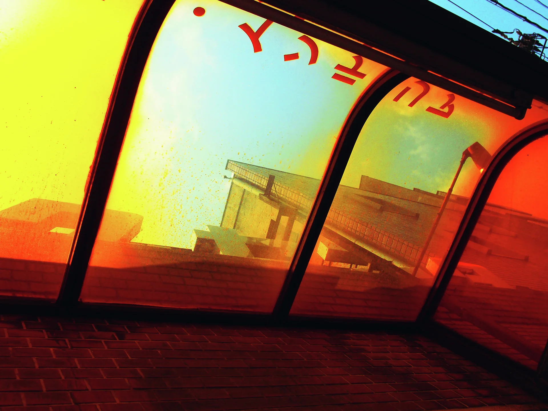 Orange and yellow translucent window panels curve above a dark brick wall, reflecting nearby buildings.