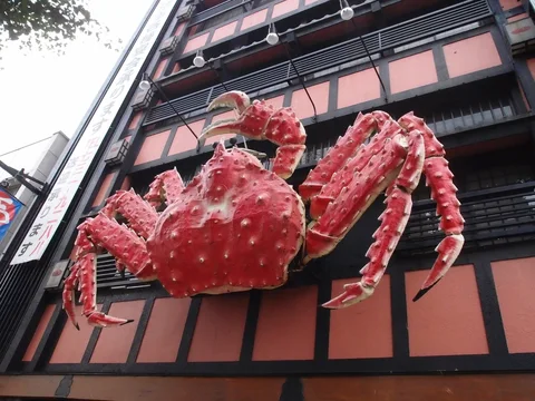 A giant red crab sculpture projects from a pink building with dark timber-patterned framing.