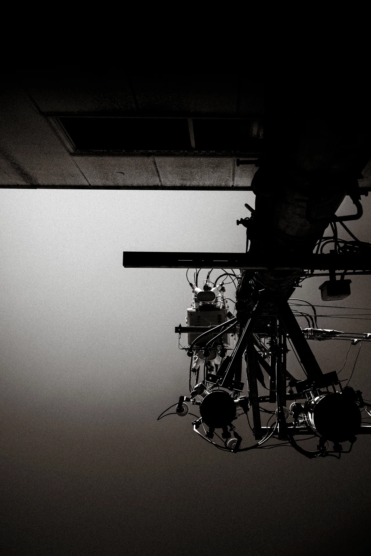 A silhouetted utility pole and clustered cables project beside a building against a gray sky.