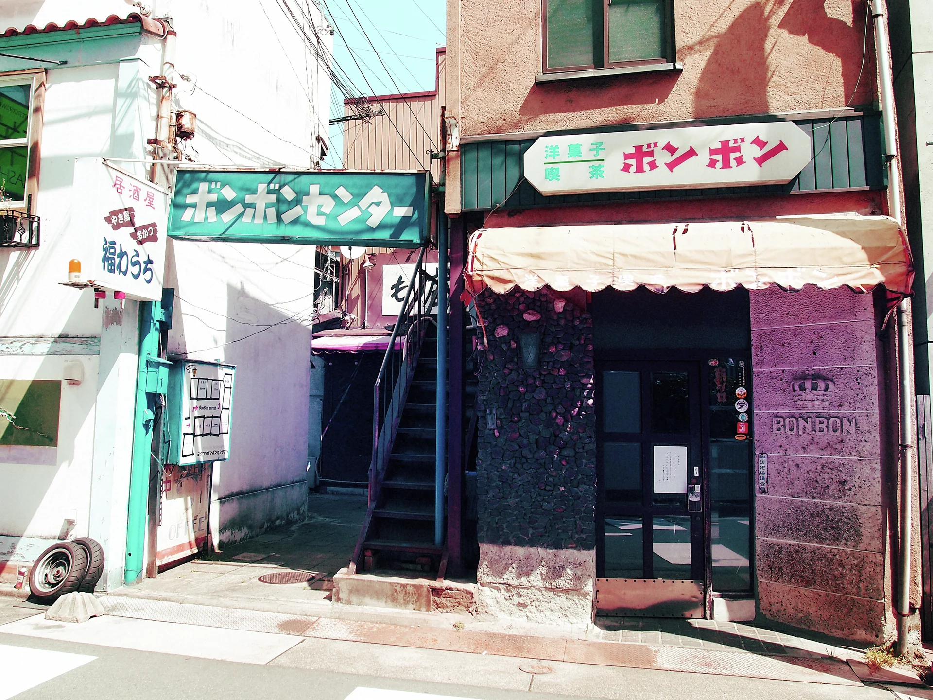 A narrow pink-toned cafe entrance sits beneath a pale scalloped awning beside an exterior staircase.