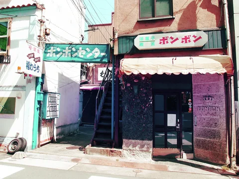 A narrow pink-toned cafe entrance sits beneath a pale scalloped awning beside an exterior staircase.