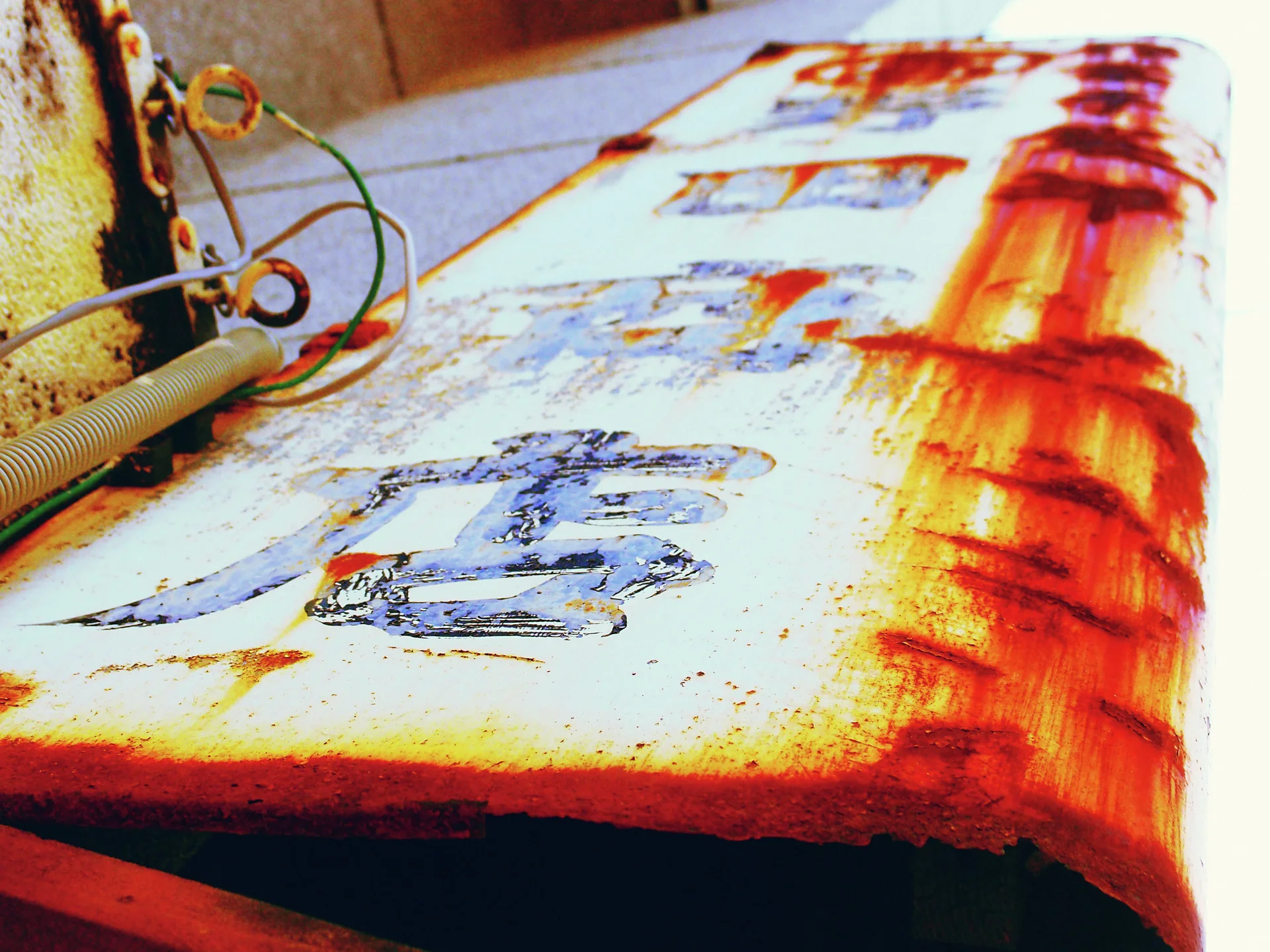 A steep close view follows a pale projecting sign with faded characters and thick orange rust.