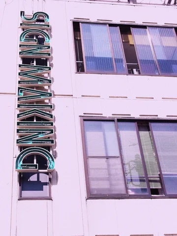 Vertical Signmaking lettering projects beside windows on a pale pink building facade.