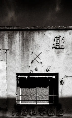 Dark stains and scattered markings cover a pale wall around a small barred opening in black and white.