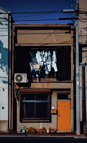 Laundry hangs in an upper window of a narrow building above an air conditioner and orange door.