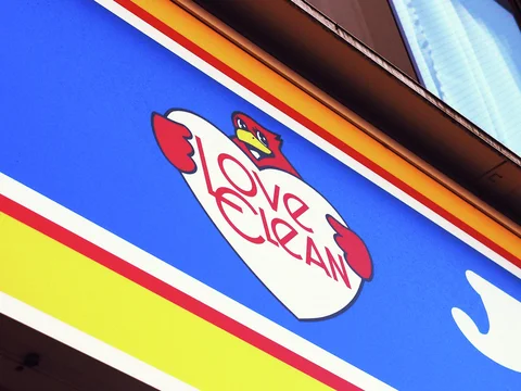 A cartoon bird surrounds red Love Clean lettering on a blue sign with yellow and red borders.
