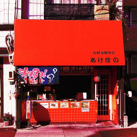 A broad red awning shelters a small open food counter faced with red tiles and illustrated signage.