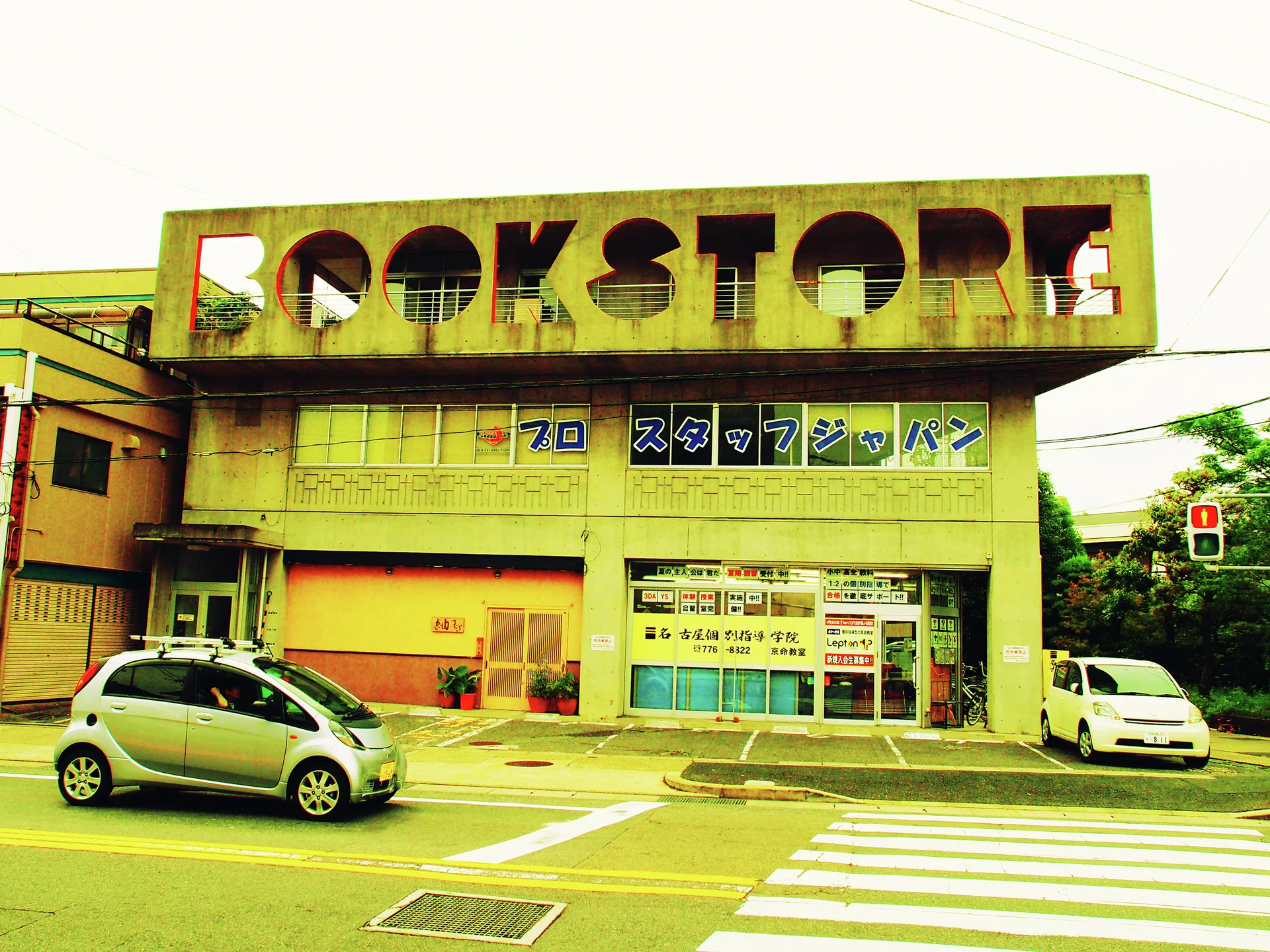 Large cutout Book Store lettering tops a low building beside passing cars and a striped pedestrian crossing.