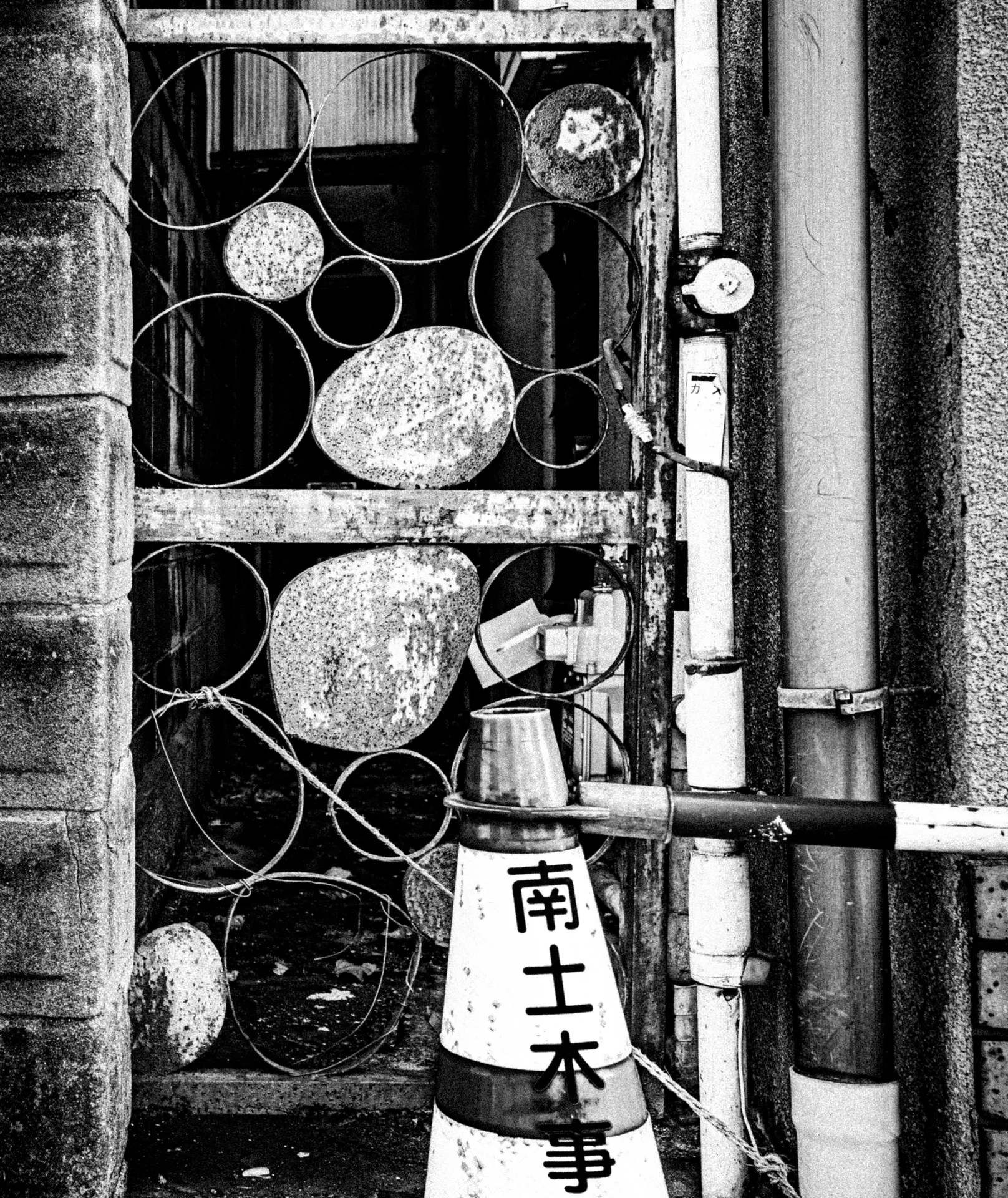 A decorative metal grille with circular motifs stands beside pipes and a labeled cone in black and white.