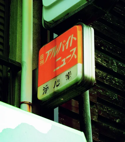 An orange and cream Japanese sign projects beside dark brickwork and a vertical metal pipe.