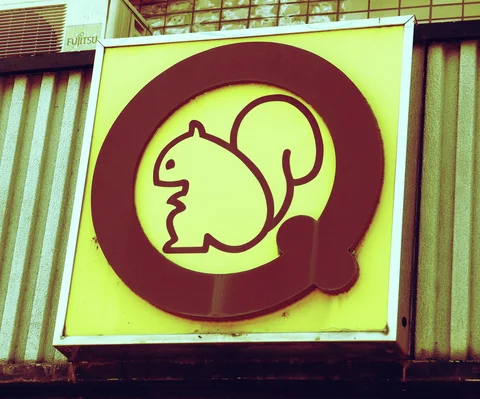 A simple squirrel silhouette sits within a thick maroon circular emblem on a pale yellow sign.