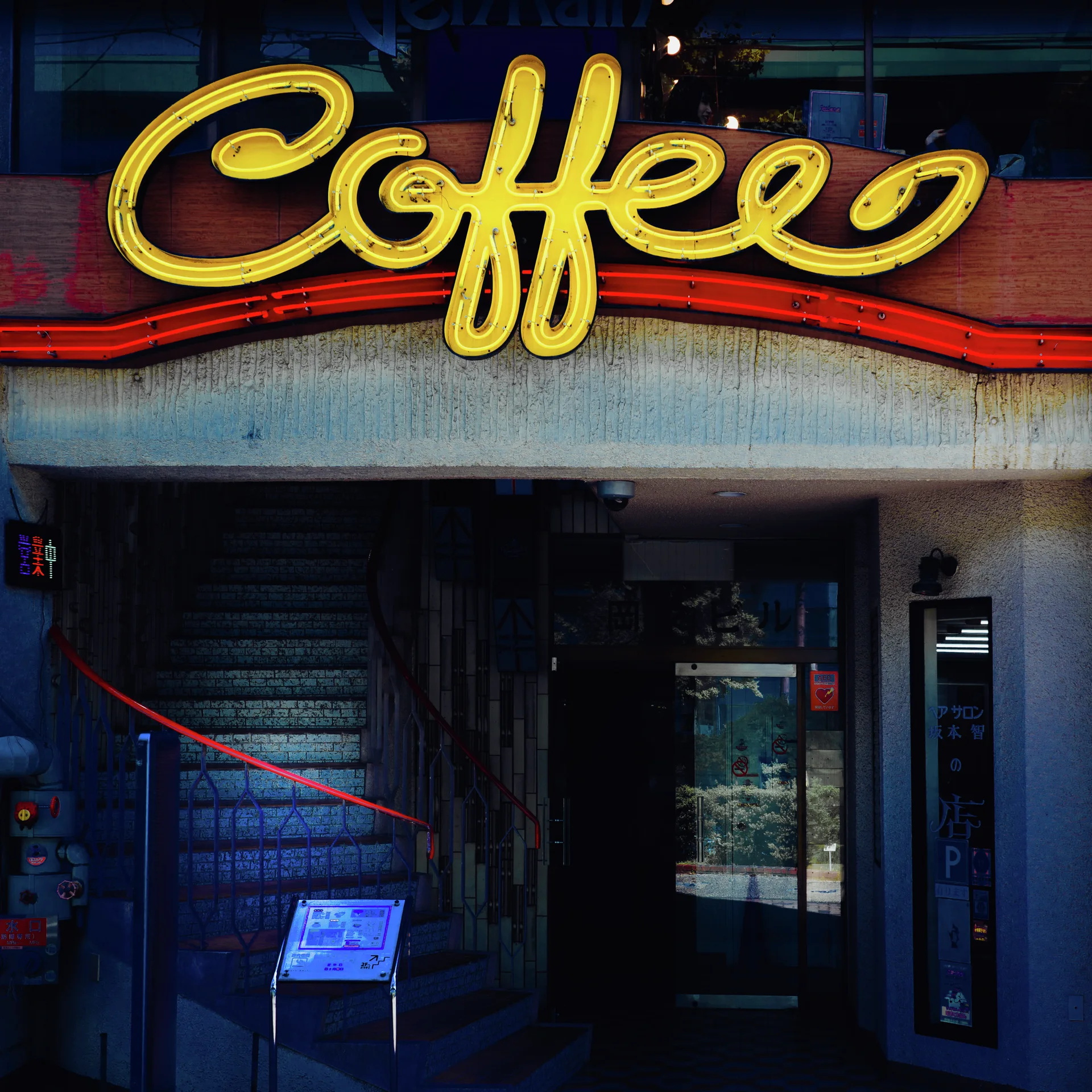 Large yellow cursive Coffee lettering hangs above a dark entrance bordered by red trim.