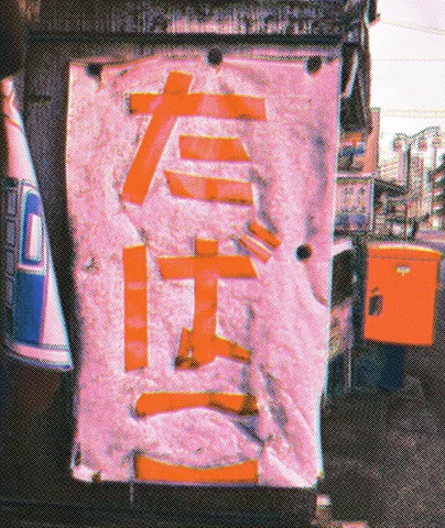 Large orange characters cover a weathered pink vertical sign beside an orange postbox.