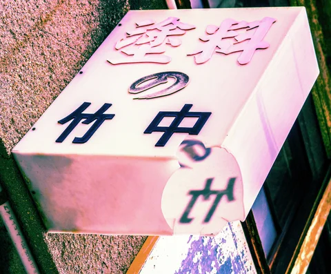A pale pink box sign with dark Japanese characters projects from a textured wall.