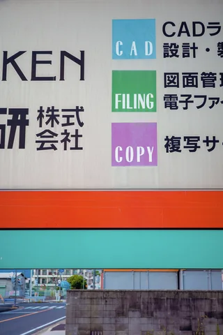 A large sign combines Japanese lettering and three colored English labels above orange and turquoise horizontal bands.