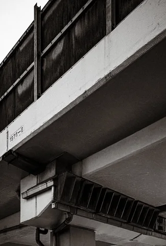 Angular concrete ledges project above a metal cable tray on a building facade in black and white.