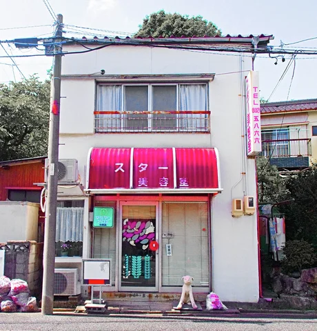 A bright red curved awning shades a narrow white shop beneath an upper window and metal balcony.