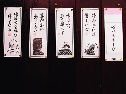 Five narrow paper notices with Japanese calligraphy and small illustrations hang against a dark wooden wall.
