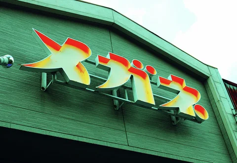 Large yellow and orange Japanese characters project from a curved green building facade.