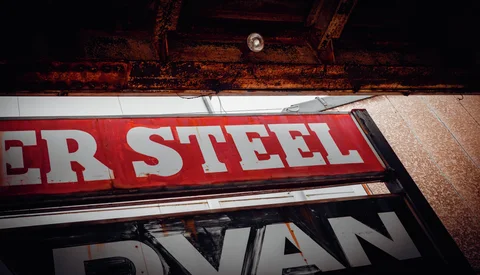 Large white Steel lettering fills a red sign beneath weathered timber and a small ceiling light.