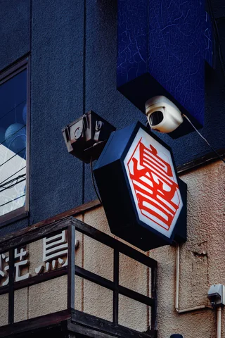A red character sign and white lantern project from a blue-toned building corner.