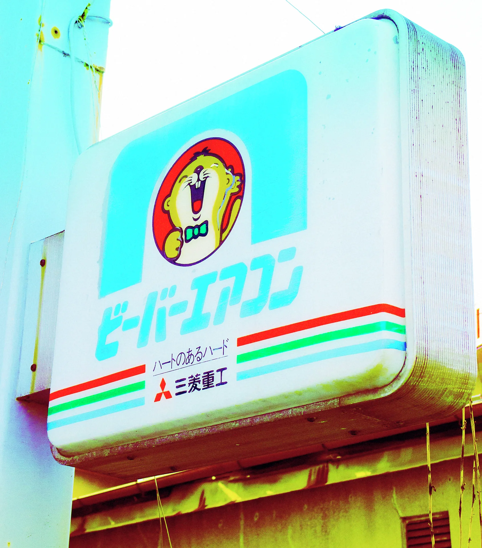 A pale blue and white projecting sign displays a smiling cartoon figure above colored horizontal stripes.