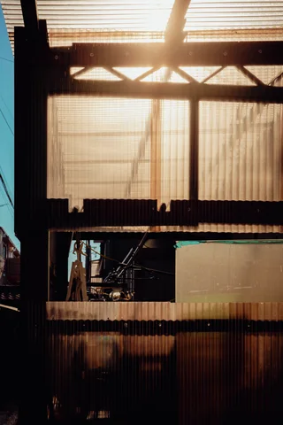 Sunlight shines through translucent corrugated panels framed by dark beams and a small rectangular opening.