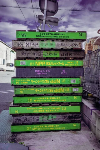 A tall stack of weathered pallets with bright green painted ends stands beneath a cloudy purple sky.