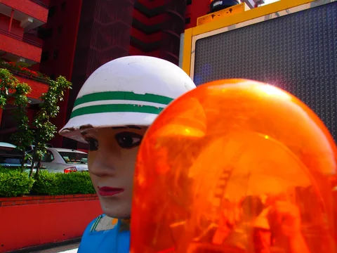 An orange beacon fills the foreground beside a mannequin's face and green-striped white helmet.