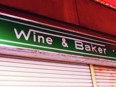 Pale wine and baker lettering runs across a dark green sign above closed white shutters.
