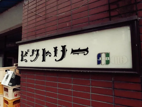 Black Japanese lettering fills a pale framed sign mounted on a reddish brick wall.