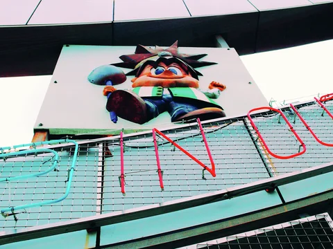 A colorful cartoon figure with spiky hair sits above a curved railing decorated with neon tubing.