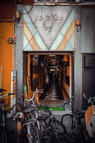 Bicycles crowd a narrow tiled entrance beneath a triangular decorative panel leading into a dim passage.
