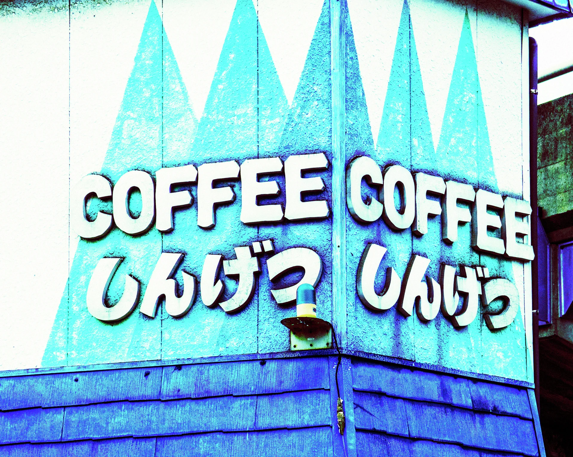 Raised white COFFEE lettering and Japanese characters span a corner wall painted with turquoise triangles.